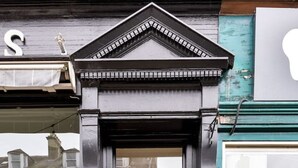 Una puerta negra con un ventanal pequeño y un adorno en la parte superior.