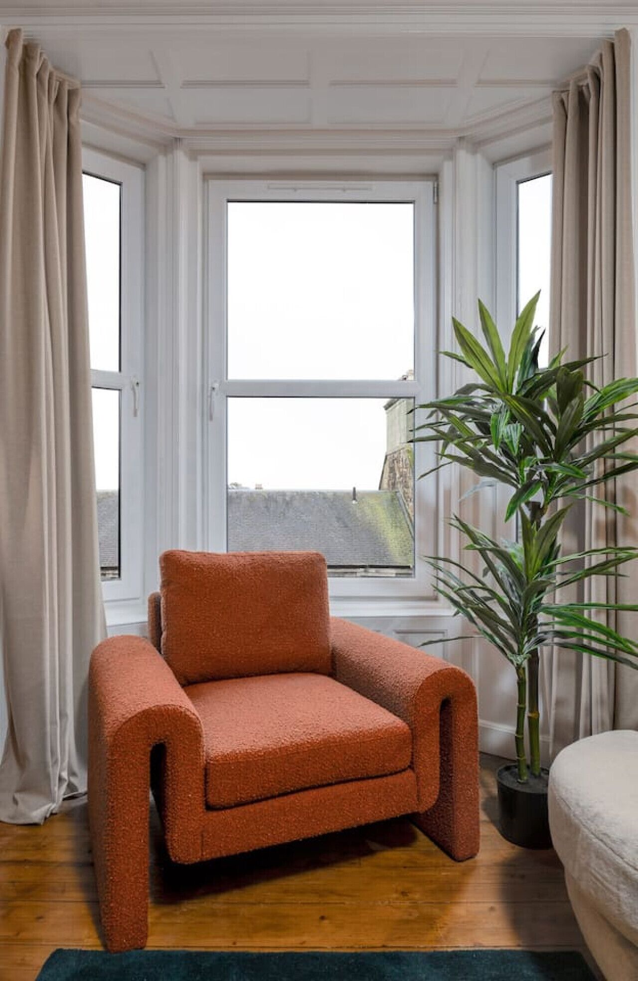 Een knus ogende kamer met een raam, een bloempot en een zachte oranje fauteuil.