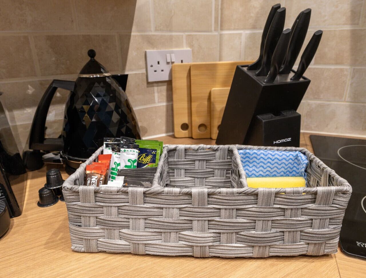 A kitchen with a woven basket containing coffee pods and a sponge.