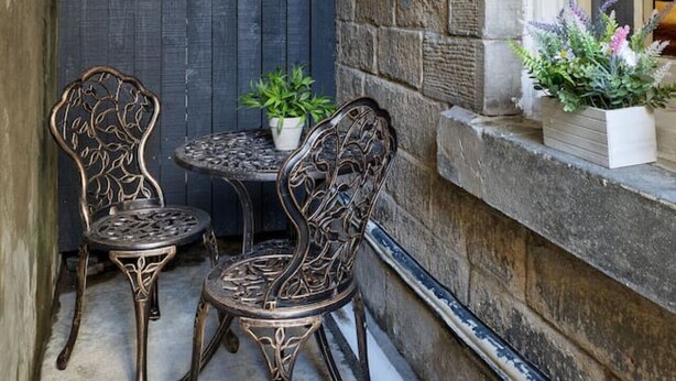 A narrow outdoor seating area with two ornate metal chairs and a small round table, a potted plant, and a stone wall. - Sapphire Suite The Stirling Residence (Stirling)