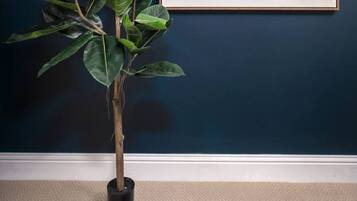A room with a dark blue wall, a framed abstract painting, and a potted plant.