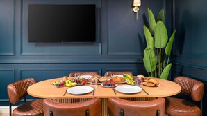 A dining area with a round table set for two, surrounded by leather chairs, with a large plant and a wall-mounted TV above. - Sapphire Suite The Stirling Residence (Stirling)