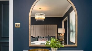 A white dresser with a large mirror above it, a potted plant, and a small table with a lamp. - Sapphire Suite The Stirling Residence (Stirling)