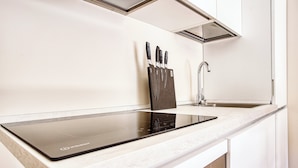 A modern kitchen with a black induction cooktop, a stainless steel faucet, and a knife block on the countertop. - JOIVY Cute Central Studio (Milan)