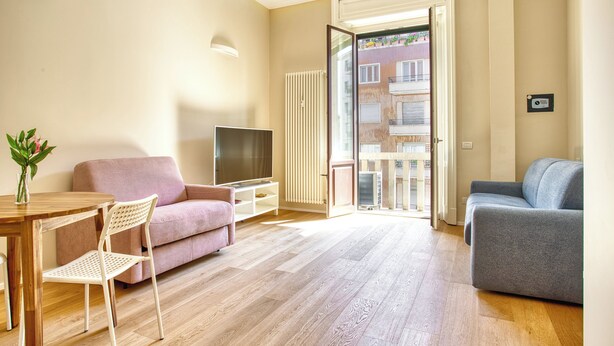 A living room with a wooden floor, a pink sofa, a blue sofa, a TV, and a dining table with chairs. - JOIVY Cute Central Studio (Milan)