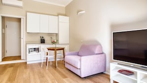 A modern living room with a flat-screen TV, a pink sofa, a wooden dining table, and white cabinetry. - JOIVY Cute Central Studio (Milan)