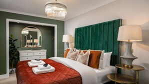 A hotel room with a large bed, a green headboard, two bedside lamps, a mirror, a dresser, and a chandelier. - Emerald Suite, The Stirling Residence (Stirling)