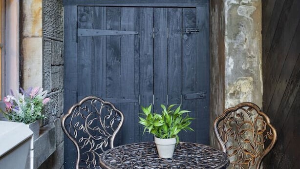 A dark wooden door with a window above it, a small round table with a potted plant, and two ornate chairs. - Emerald Suite, The Stirling Residence (Stirling)