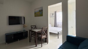 A modern living room with a flat-screen TV, a dining table with chairs, a blue sofa, and a painting on the wall. - Charming 1 bedroom apartment with AC, WiFi in lovely Lapu-Lapu City (Lapu-Lapu City)