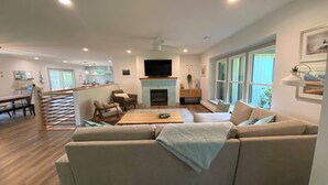 A spacious living room with a large sofa, a fireplace, and a dining area with a kitchen in the background.