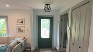 A hallway with a wooden floor, a beige sofa, a door with a window, and a closet with sliding doors.
