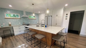 A modern kitchen with a large island, bar stools, white cabinetry, and a wooden floor.