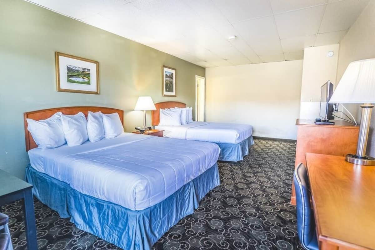 A hotel room with two beds, a desk, and a TV.