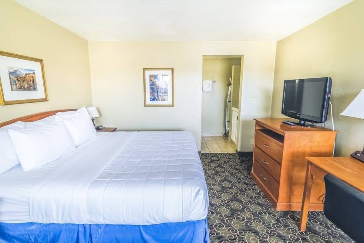 A hotel room with a large bed, a wooden dresser, a television, and a framed picture on the wall.