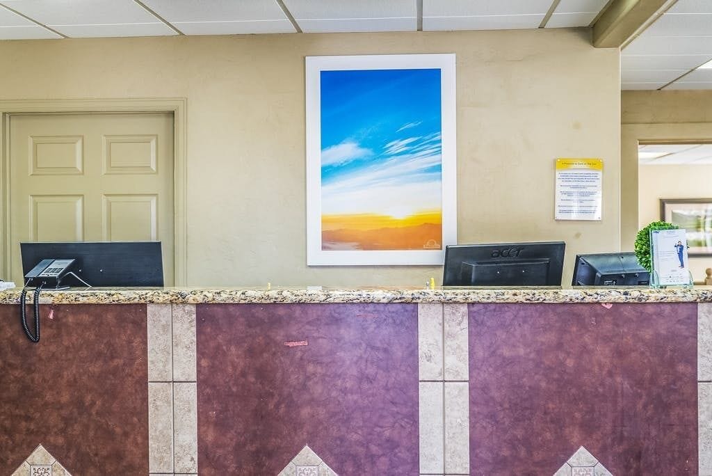 A reception desk with a computer, a phone, and a framed picture of a sunset.