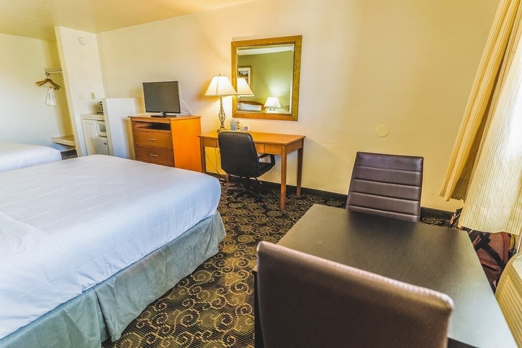 Habitación de hotel con dos camas, un escritorio con silla, televisor, lámpara y espejo.