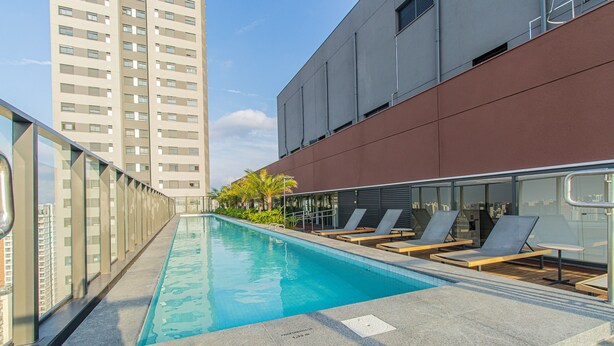 A rooftop pool with lounge chairs and a view of a high-rise building. - Cozy Refuge Near Allianz Parque Sp-p1504a (São Paulo)