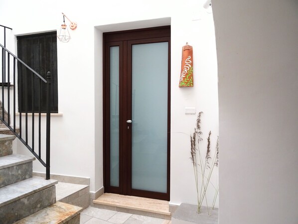 A modern entrance with a glass door, a staircase, and a small outdoor area with plants.
