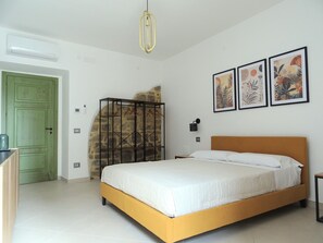 A bedroom with a bed, a green door, a stone wall, and two framed floral artworks.