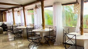 A restaurant with round tables and chairs, large windows with curtains, and a tiled floor. - Pousada Encantos da Serra Macacos (Nova Lima)