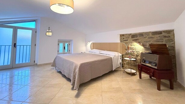Ruime slaapkamer met een groot bed, een accentmuur van steen, een televisie en een balkon met glazen deuren.