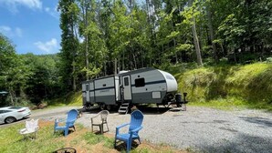 A recreational vehicle (RV) parked on a gravel path surrounded by lush greenery.