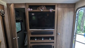 A compact living space with a large flat-screen TV mounted on a wooden wall, a fireplace below, and a door leading to a garage.