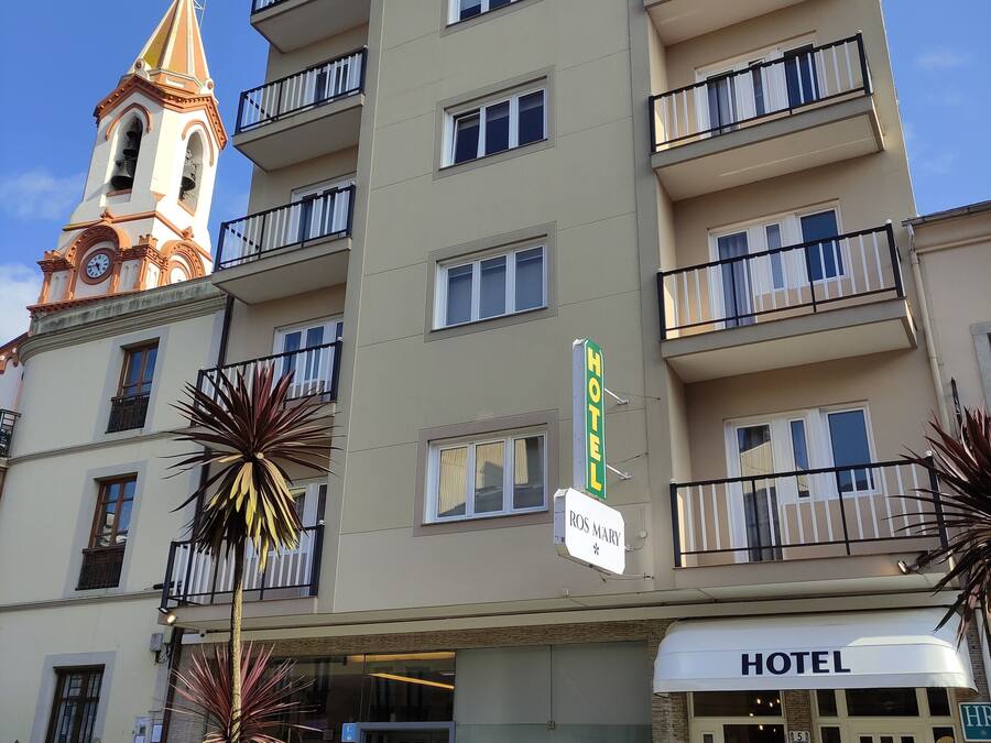 A hotel with a prominent clock tower, multiple balconies, and a sign indicating 'HOTEL'.