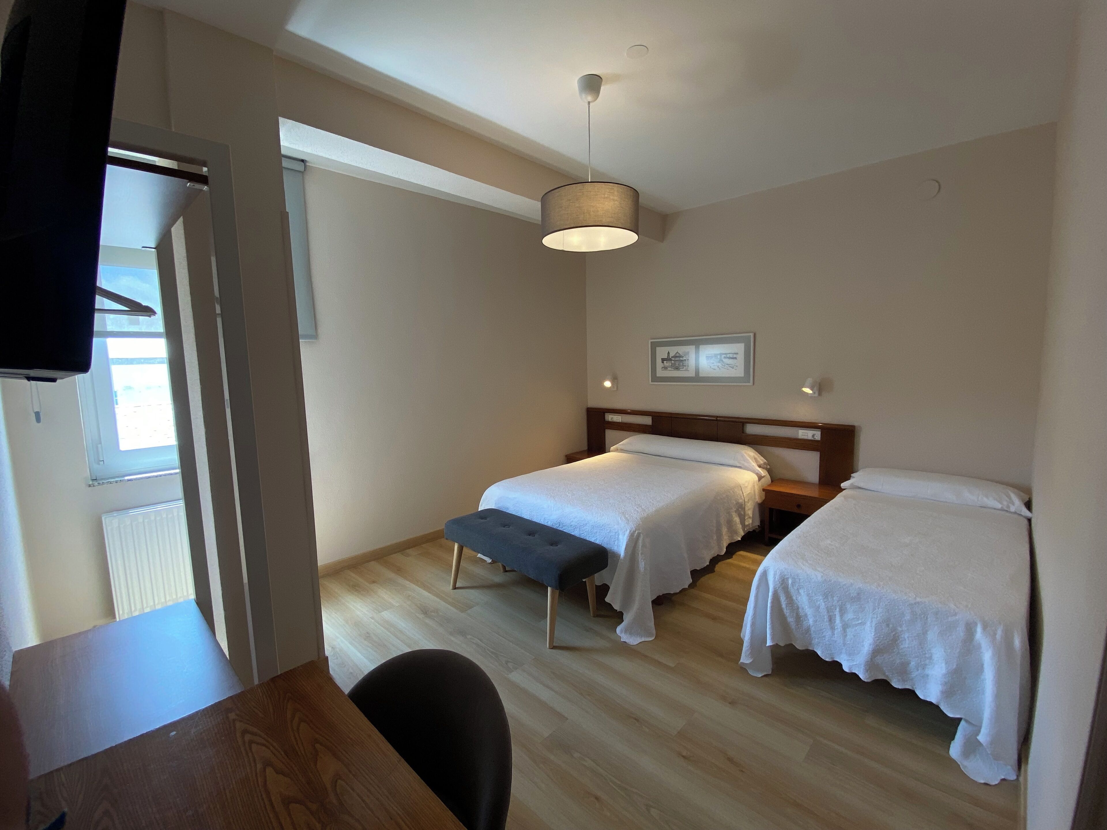 Een hotelkamer met twee enkele bedden, een houten bureau, een stoel, een plafondlamp en een raam.