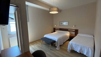 Een hotelkamer met twee enkele bedden, een houten bureau, een stoel, een plafondlamp en een raam.