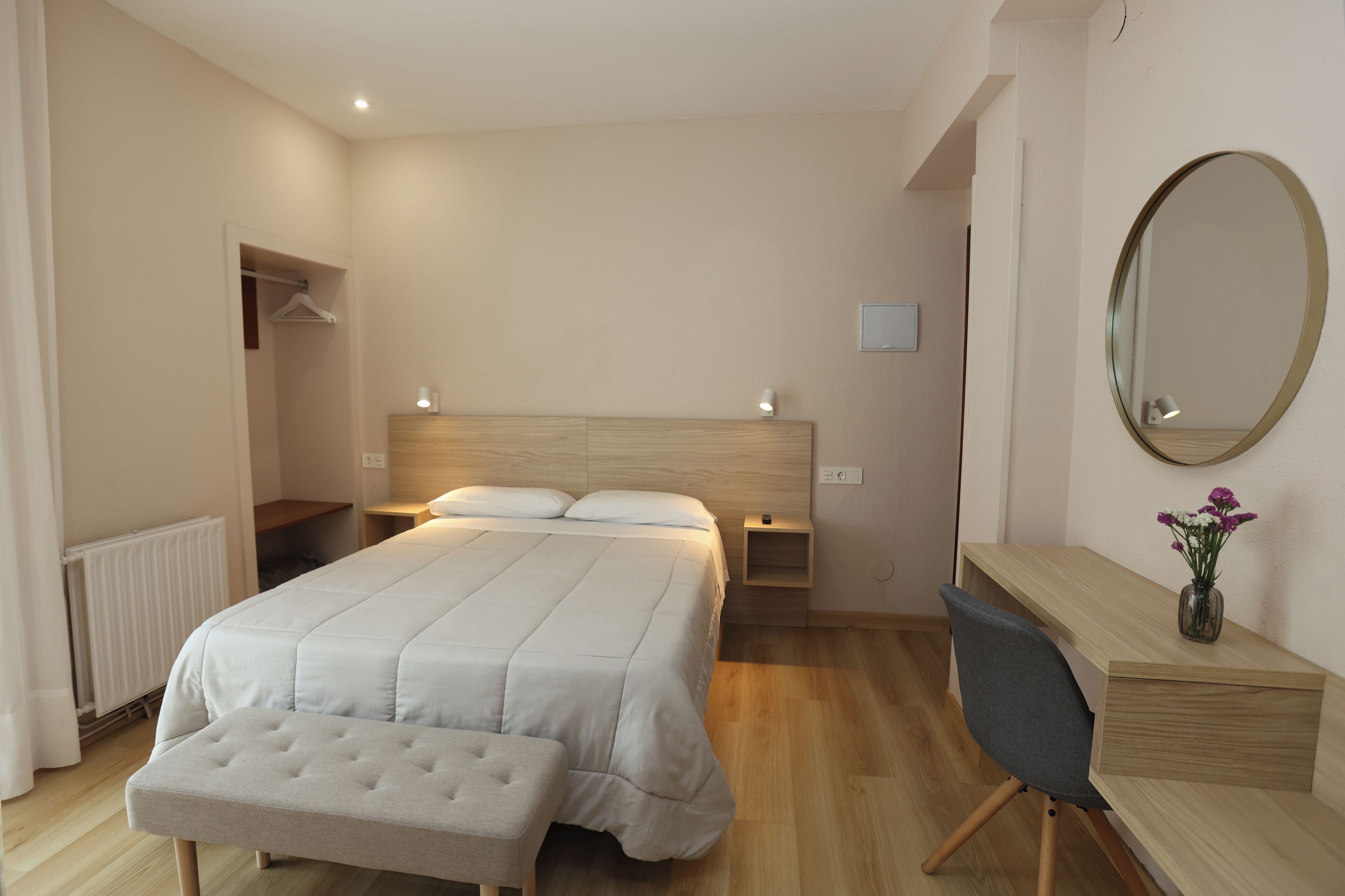 Un dormitorio con cama, mesita de noche, silla y escritorio con espejo.