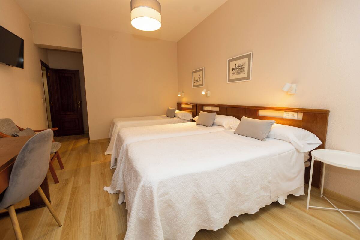 Ein Hotelzimmer mit zwei Betten, Holzboden, einem kleinen Tisch und einem an der Wand befestigten Fernseher.