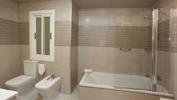 Un baño moderno con inodoro, bidé y ducha con mampara de vidrio.