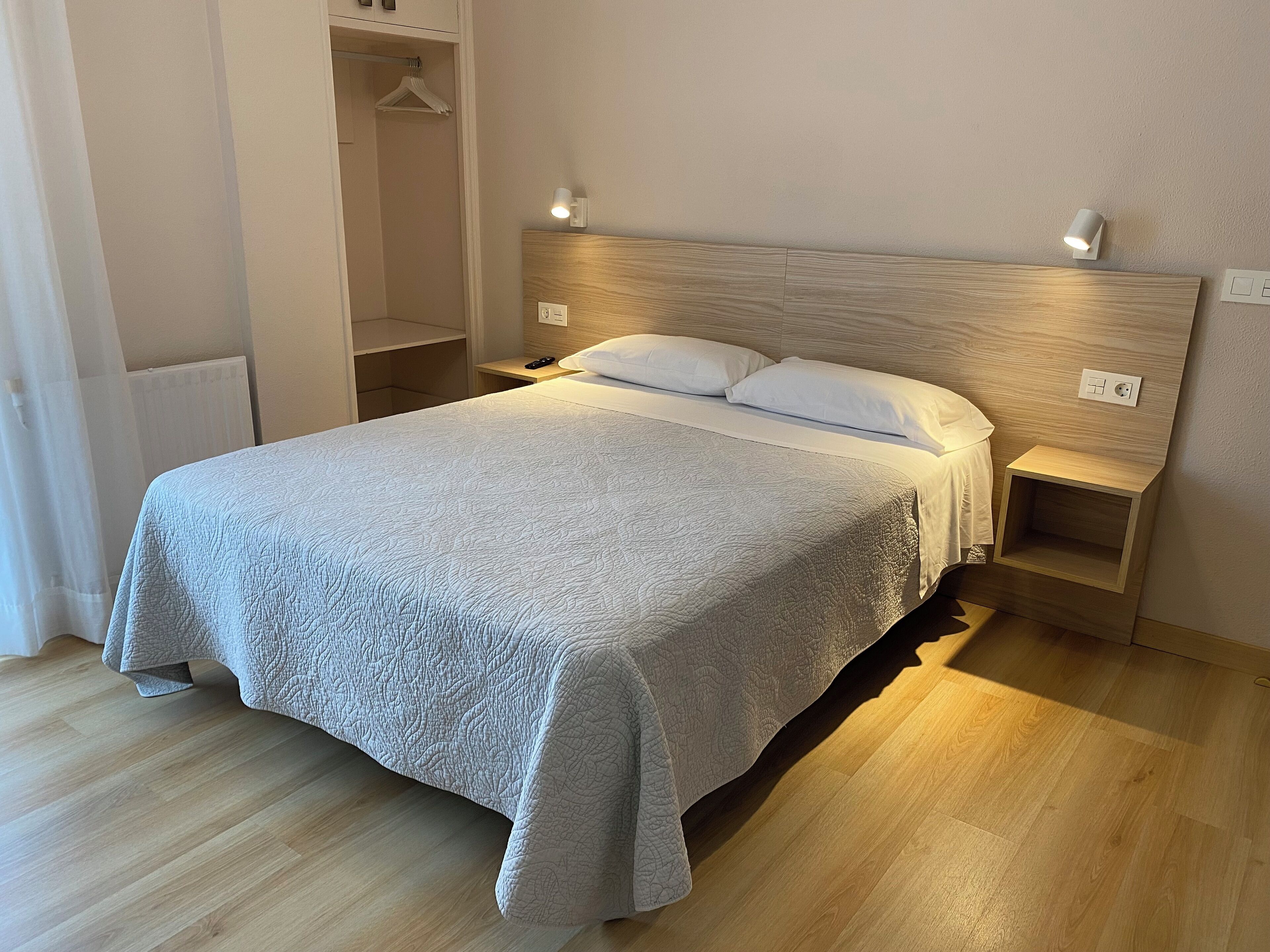 A neatly made bed with a quilted cover, two bedside tables with lamps, and a wooden headboard.