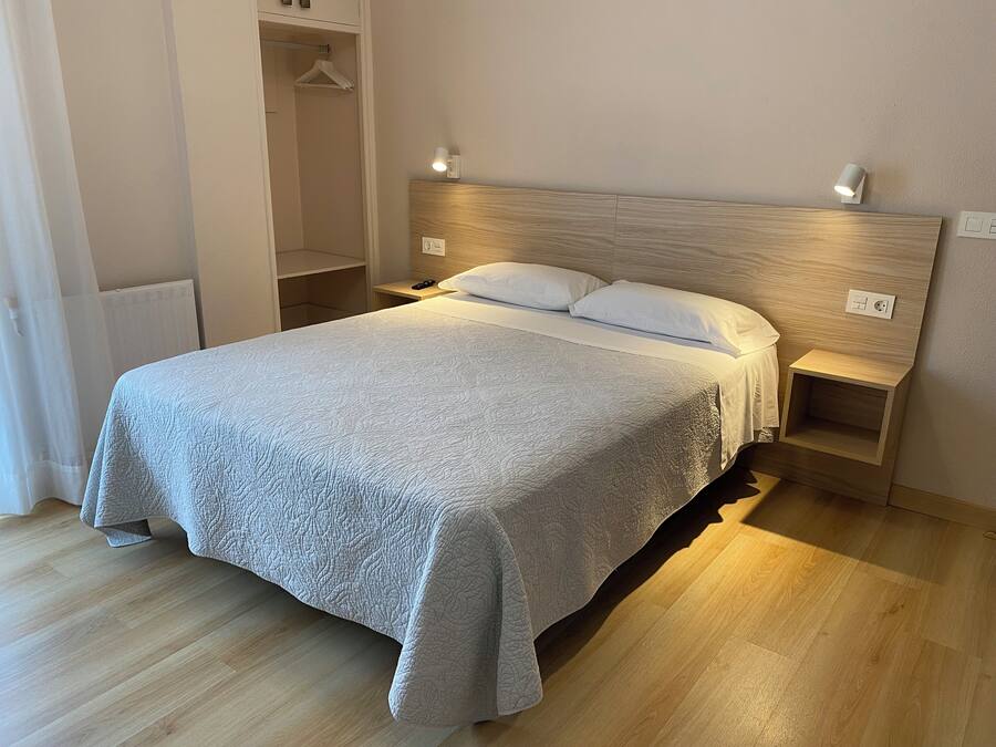 Un lit bien fait, recouvert d’une courtepointe matelassée, deux tables de chevet avec des lampes et une tête de lit en bois.