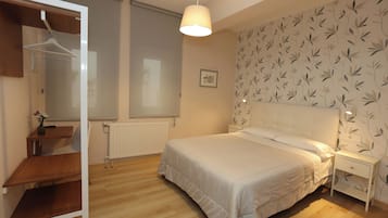 A bedroom with a bed, a bedside table, a hanging light fixture, a radiator, and a wardrobe.