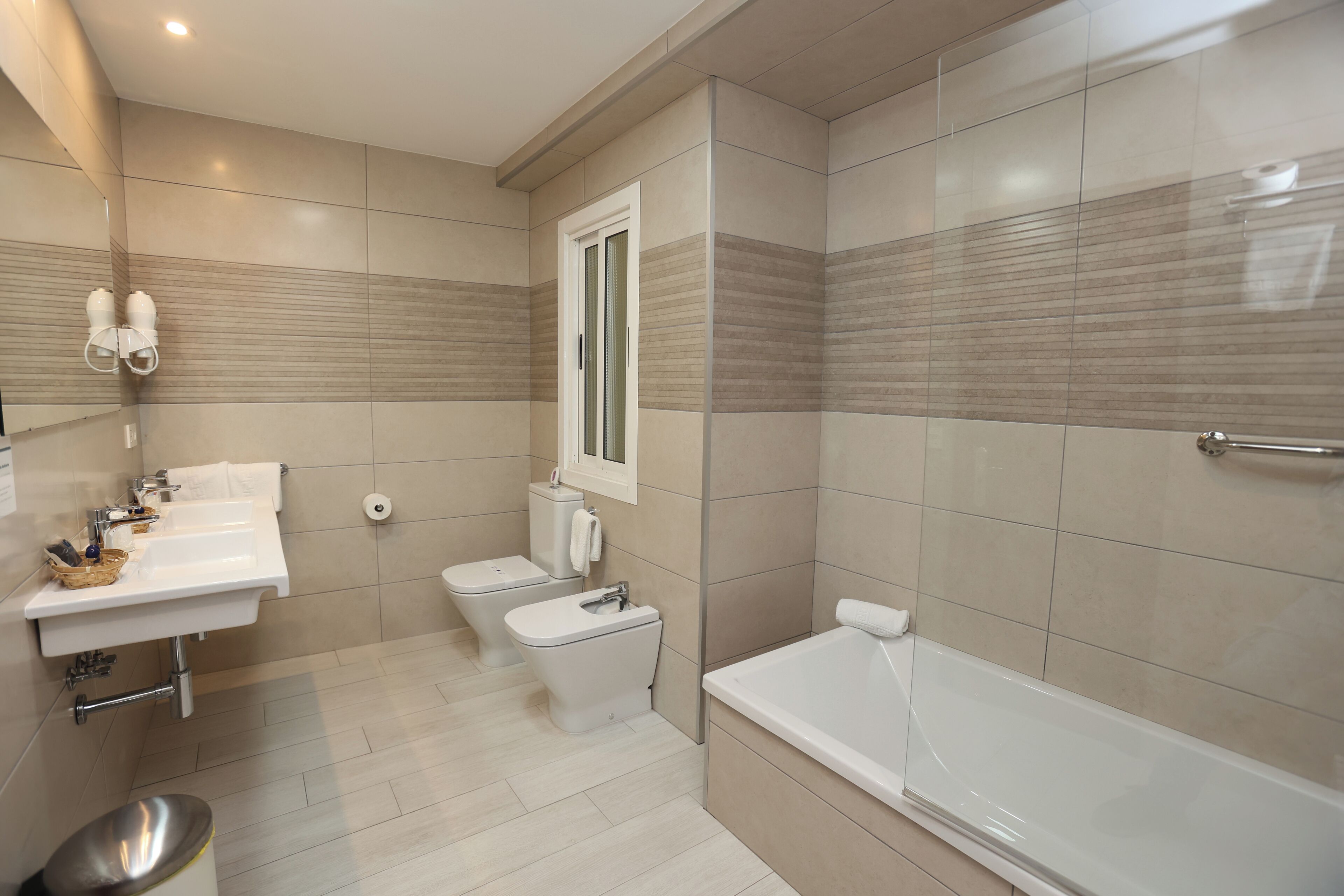 Un baño moderno con un lavamanos, dos inodoros y una bañera.