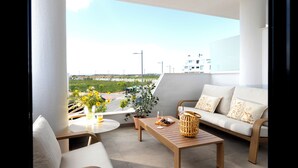 A balcony with a sofa, a table, and a chair. There is a view of a road and buildings in the background. - Cozy furnished apartment on resort with unique swimming lake (19200)