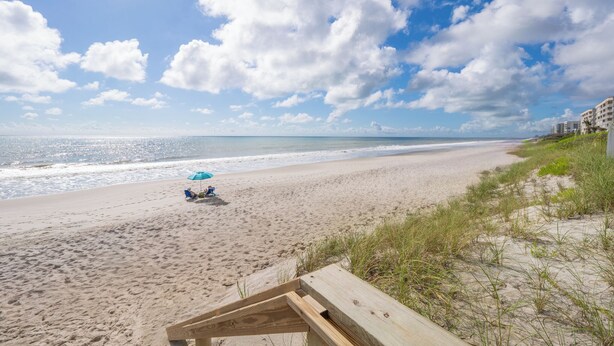 A beach with a wooden deck, a beach umbrella, and a clear sky.