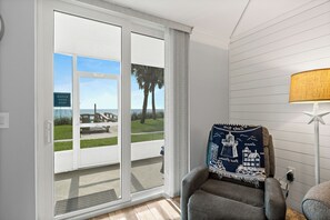 Una habitación con vista a la playa, una silla con un cojín de temática náutica y una lámpara.