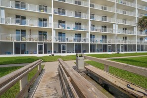 A multi-story hotel with balconies, a grassy courtyard, and a wooden bridge.