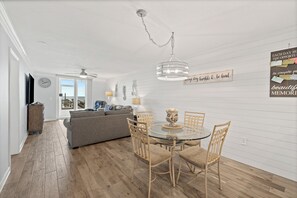 Ein modernes Wohnzimmer mit einem Glastisch, Korbstühlen, einem grauen Sofa und einem Deckenventilator.