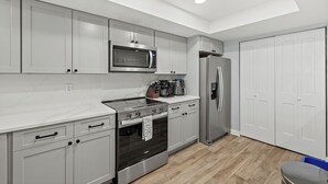 A modern kitchen with grey cabinets, a stainless steel microwave, a built-in oven, a refrigerator, and a coffee maker.