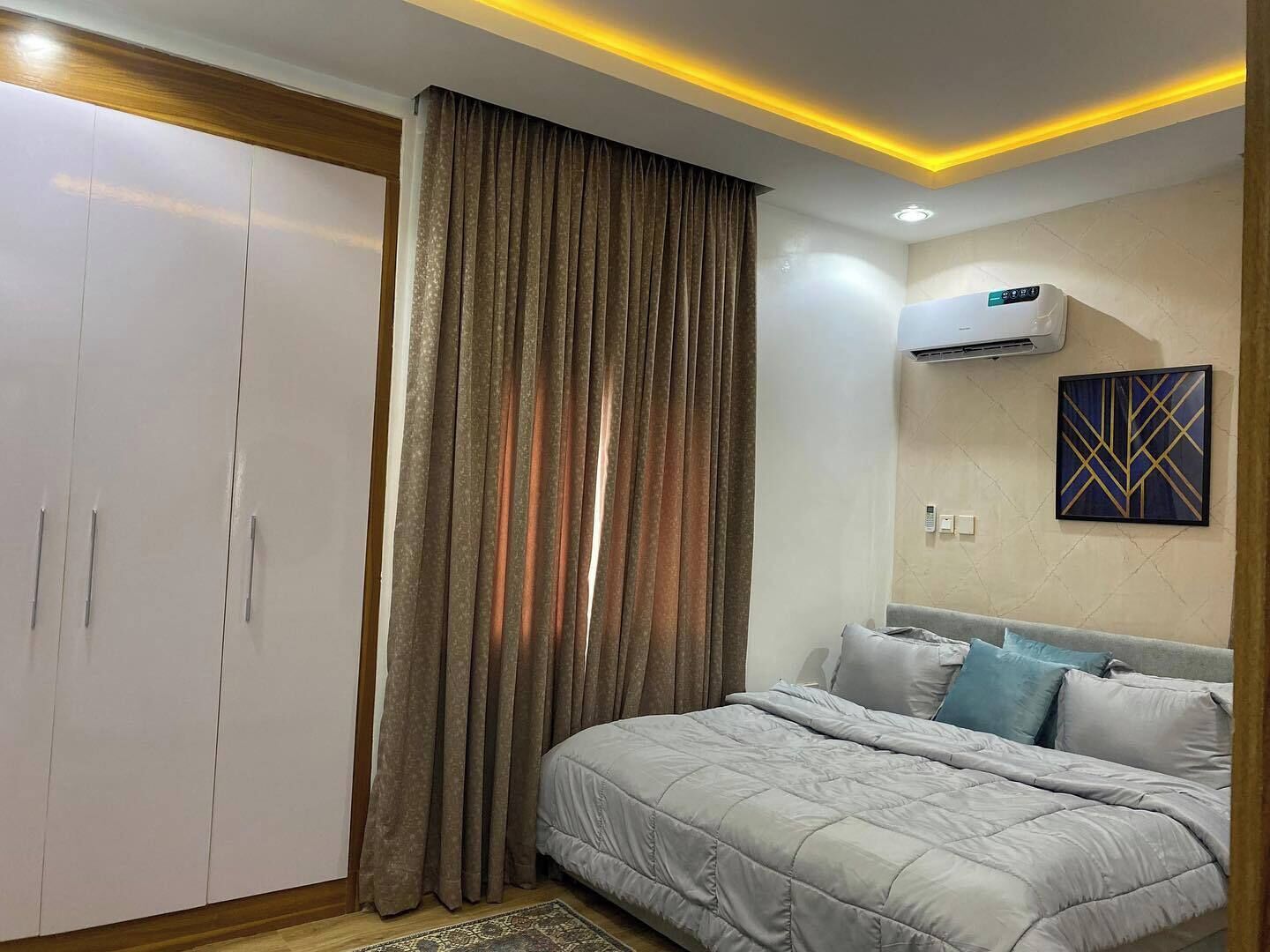 A bedroom with a bed, a wardrobe, a curtain, an air conditioner, and a wall-mounted artwork.