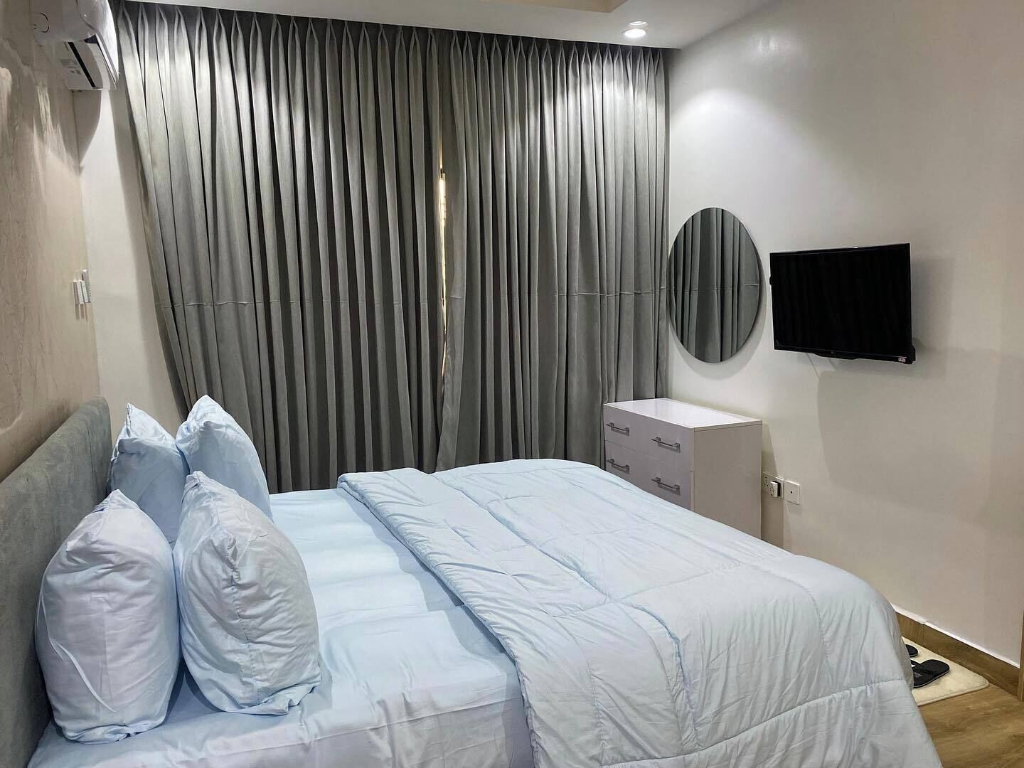 Una camera da letto moderna con un letto, una cassettiera, una televisione e una finestra con tende.