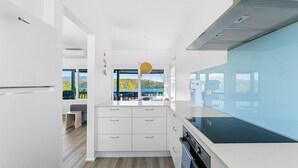 A modern kitchen with white cabinetry, a blue countertop, and a view of a lake.