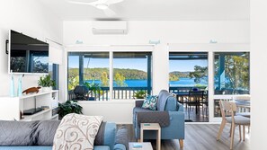 Una sala de estar moderna con un televisor grande, asientos cómodos y vistas a un lago y colinas.