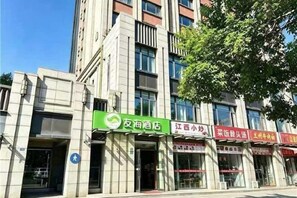 A multi-story building with commercial establishments on the ground floor, including a green sign for a hospitality service and several red signs for other businesses.