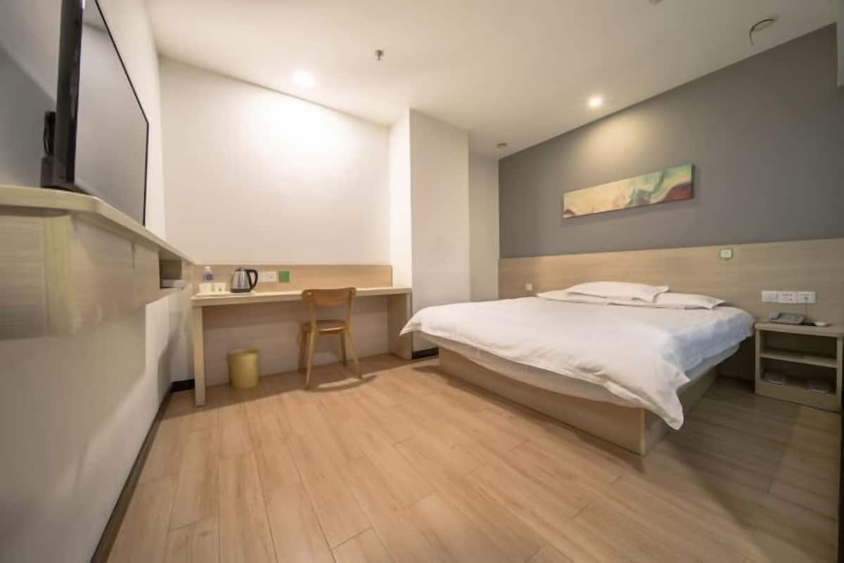 A bedroom with a bed, desk, chair, and a painting on the wall.