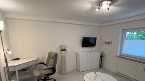 A modern room with a white desk, chair, and a marble table. There is a TV mounted on the wall and a window with blinds. - FeWo meisteroffice in Sackgässle, ground floor apartment, terrace, kitchen, near Ulm (Dornstadt)